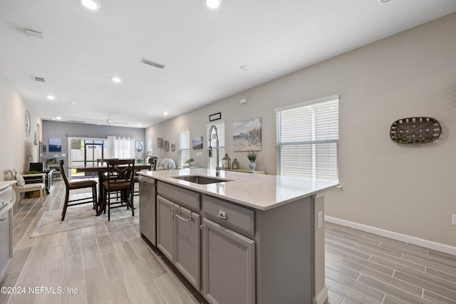 kitchen with light hardwood / wood-style flooring, a kitchen island with sink, gray cabinetry, and sink