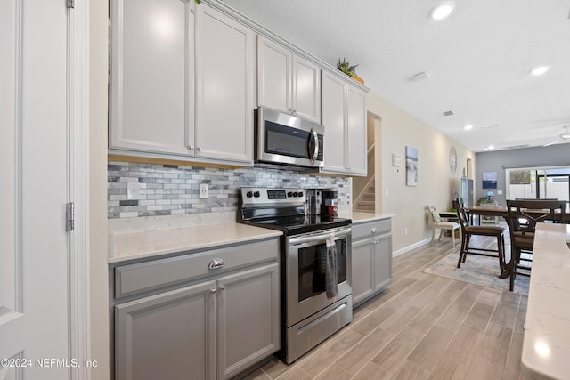 kitchen with gray cabinetry, light hardwood / wood-style flooring, decorative backsplash, appliances with stainless steel finishes, and light stone counters