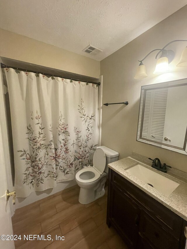 full bathroom with hardwood / wood-style floors, shower / bath combination with curtain, a textured ceiling, toilet, and vanity