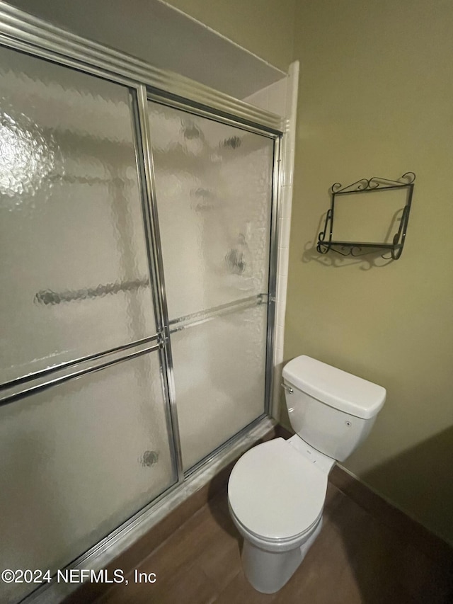 bathroom featuring toilet, a shower with shower door, and hardwood / wood-style flooring