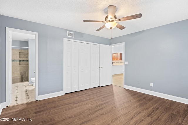 unfurnished bedroom with connected bathroom, ceiling fan, wood-type flooring, a textured ceiling, and a closet