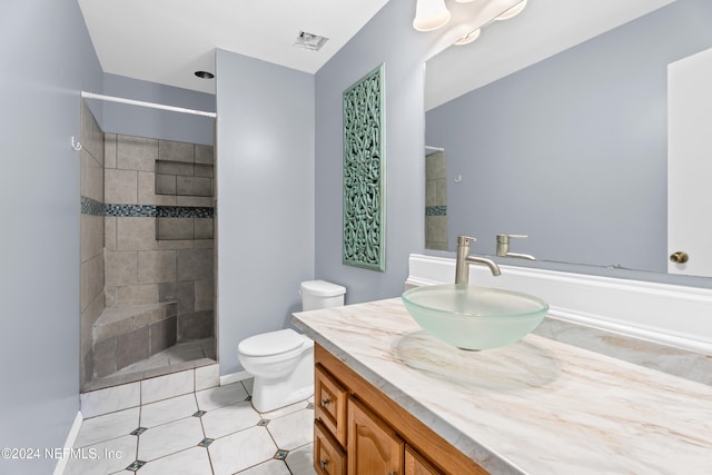 bathroom with tile patterned flooring, vanity, toilet, and a tile shower