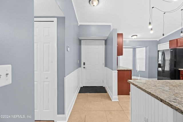 kitchen featuring ornamental molding, a textured ceiling, light tile patterned flooring, light stone counters, and black fridge with ice dispenser