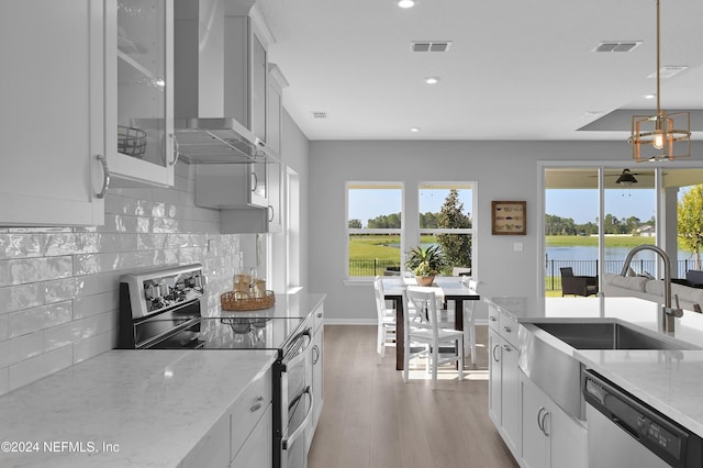 kitchen with wall chimney range hood, white cabinets, light stone counters, a water view, and appliances with stainless steel finishes