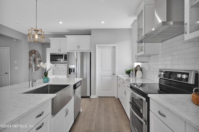 kitchen featuring white cabinets, wall chimney range hood, light hardwood / wood-style flooring, decorative light fixtures, and stainless steel appliances