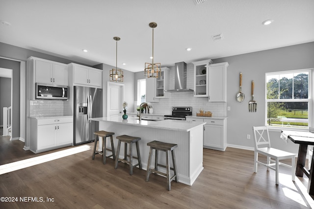 kitchen with white cabinetry, wall chimney range hood, a kitchen island with sink, and appliances with stainless steel finishes