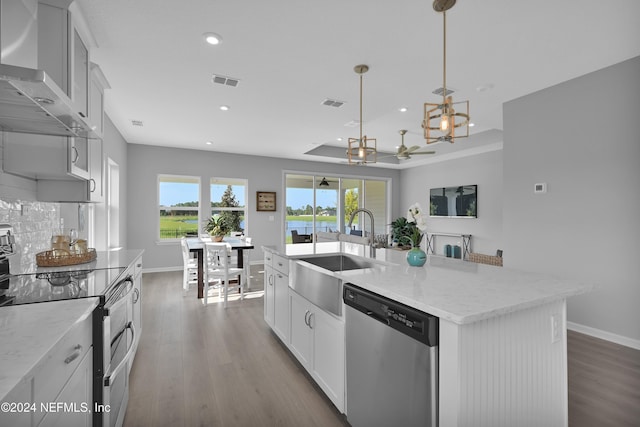 kitchen with pendant lighting, a kitchen island with sink, ceiling fan, wall chimney exhaust hood, and stainless steel appliances