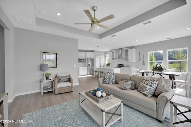 living room with hardwood / wood-style floors, ceiling fan, sink, and a tray ceiling