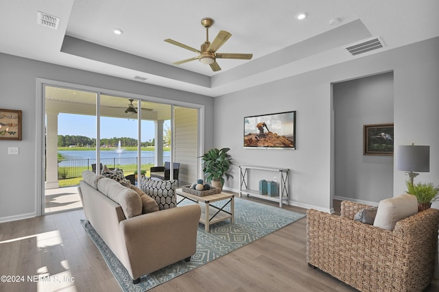 living room with hardwood / wood-style flooring, a raised ceiling, and ceiling fan