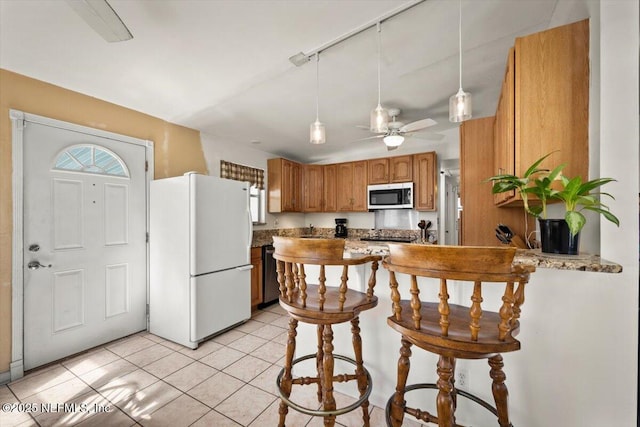 kitchen featuring a kitchen breakfast bar, ceiling fan, light tile patterned floors, white fridge, and kitchen peninsula