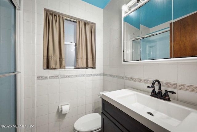 bathroom with vanity, a shower with door, decorative backsplash, toilet, and tile walls