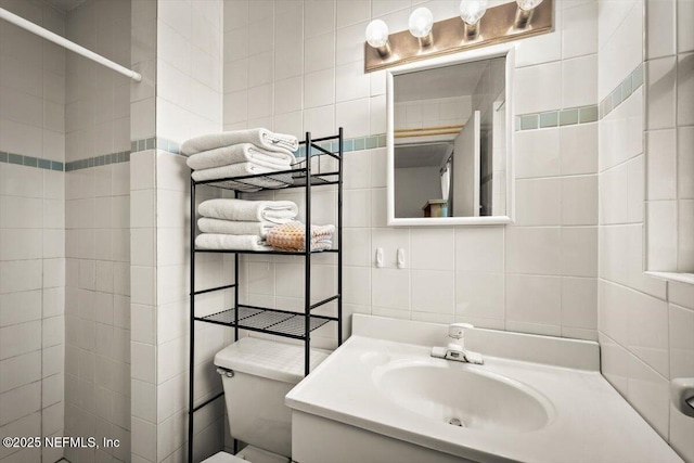 bathroom with walk in shower, vanity, toilet, and tile walls