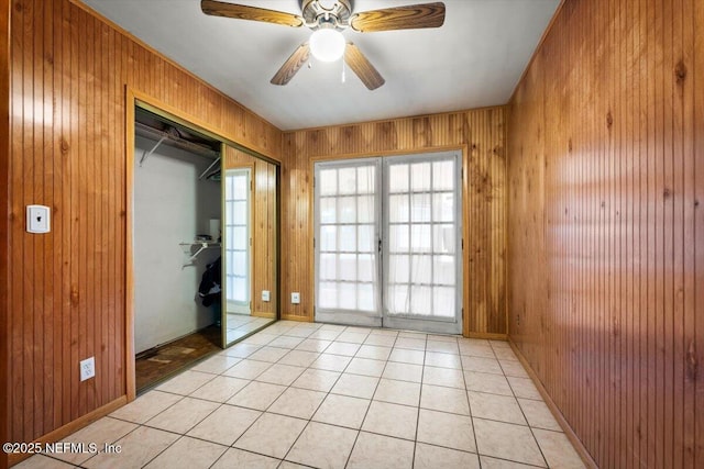 tiled spare room with ceiling fan, wood walls, and french doors