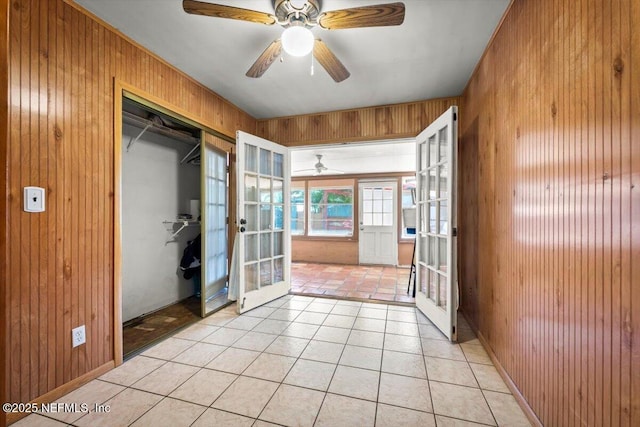 tiled spare room with wooden walls, french doors, and ceiling fan