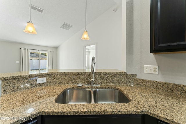 kitchen featuring lofted ceiling, sink, decorative light fixtures, and stone countertops