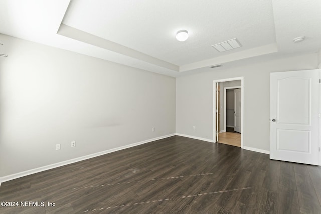 empty room with a tray ceiling, dark wood-type flooring, and a textured ceiling