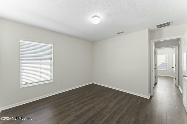 spare room with a textured ceiling, dark hardwood / wood-style floors, and a healthy amount of sunlight