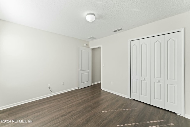 unfurnished bedroom featuring a textured ceiling, dark hardwood / wood-style flooring, and a closet