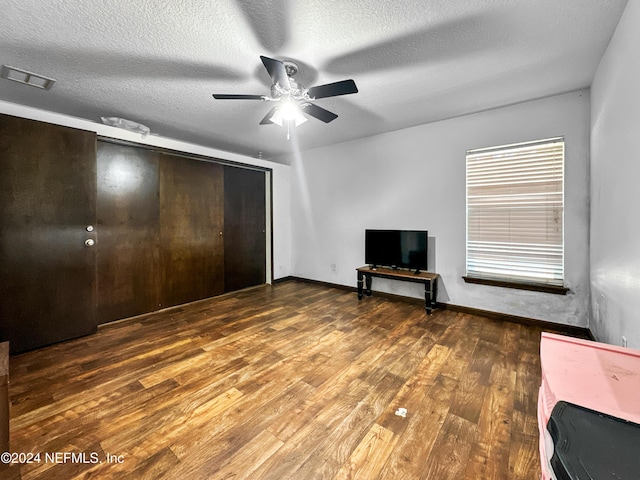 unfurnished bedroom with a textured ceiling, a closet, ceiling fan, and dark wood-type flooring