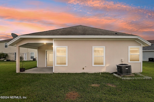 back house at dusk featuring a lawn, a patio, and central AC unit