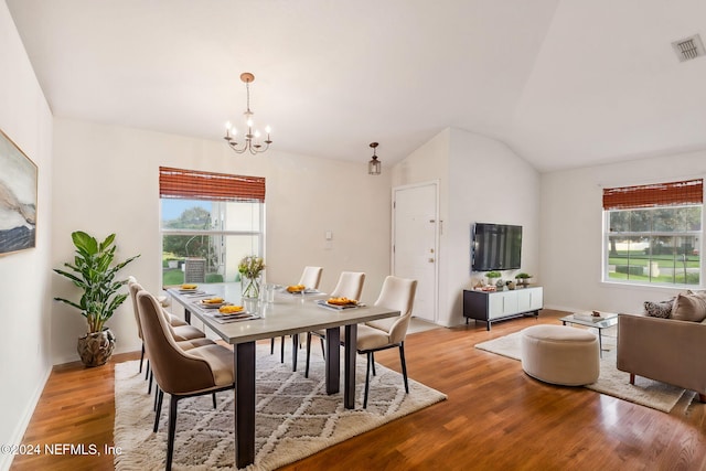 dining area with a notable chandelier, plenty of natural light, vaulted ceiling, and light hardwood / wood-style flooring