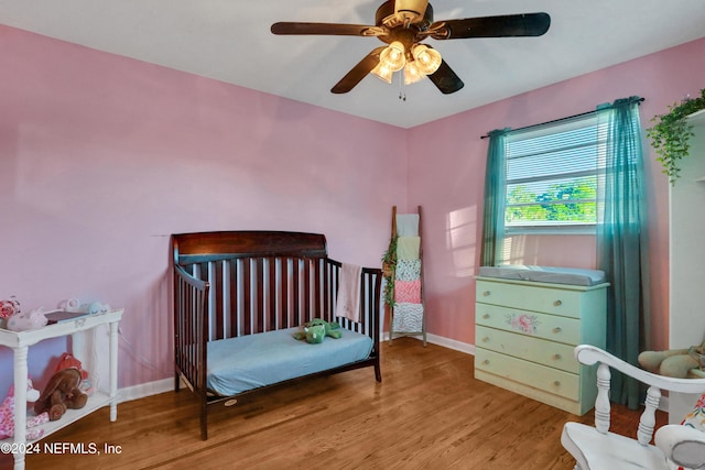 bedroom with a crib, light hardwood / wood-style flooring, and ceiling fan