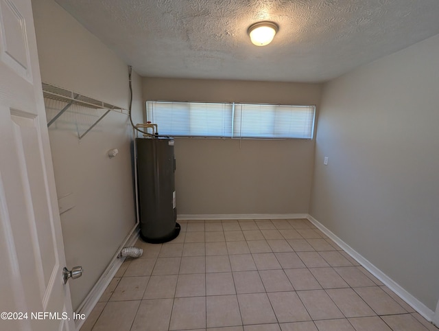 washroom featuring electric water heater, a textured ceiling, and light tile patterned floors