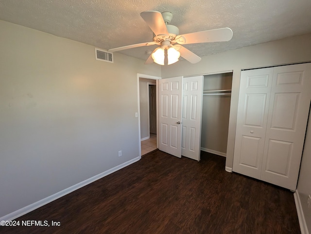 unfurnished bedroom with a textured ceiling, two closets, ceiling fan, and dark wood-type flooring