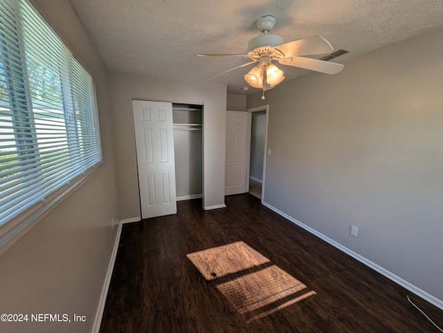 unfurnished bedroom with a textured ceiling, ceiling fan, dark wood-type flooring, and a closet