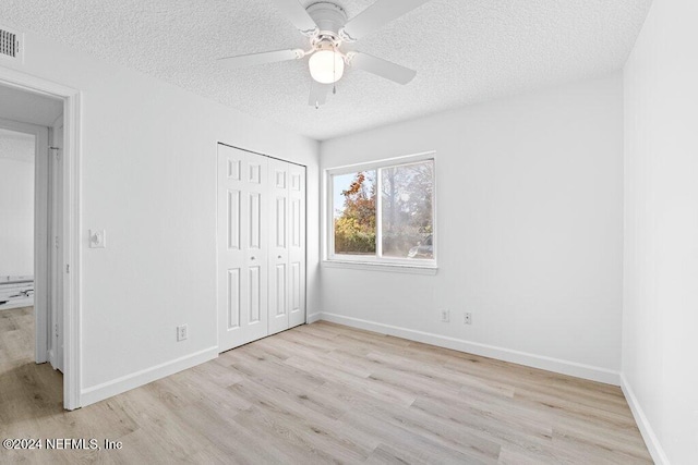 unfurnished bedroom featuring ceiling fan, a closet, a textured ceiling, and light wood-type flooring