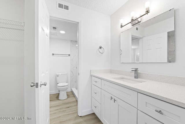 bathroom with walk in shower, vanity, a textured ceiling, wood-type flooring, and toilet