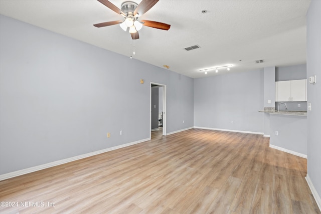 empty room with a textured ceiling, light hardwood / wood-style floors, ceiling fan, and sink