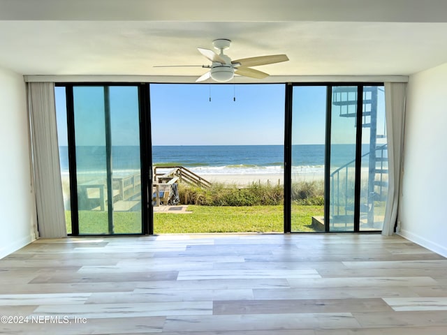 interior space with floor to ceiling windows, ceiling fan, a beach view, light hardwood / wood-style floors, and a water view