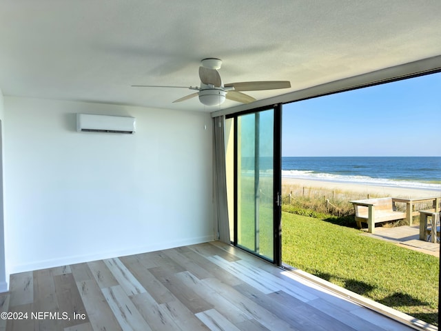 interior space with a wall unit AC, ceiling fan, a water view, and a view of the beach