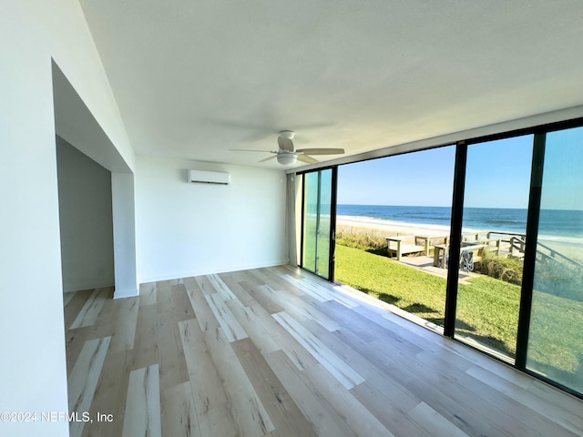 empty room featuring a healthy amount of sunlight, a water view, light wood-type flooring, and a wall mounted AC