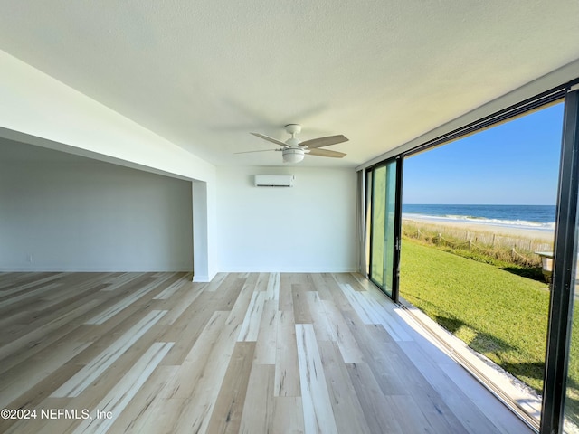 empty room with ceiling fan, a beach view, a wall unit AC, a water view, and light wood-type flooring