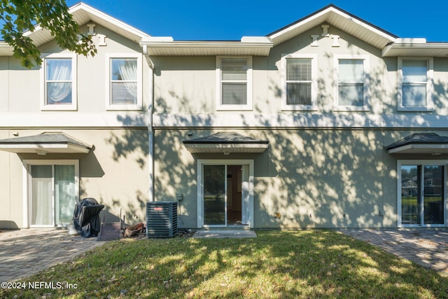 rear view of property with central AC unit and a lawn