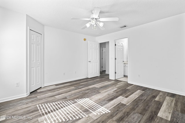 unfurnished bedroom with a textured ceiling, ceiling fan, dark wood-type flooring, and ensuite bath