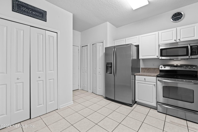 kitchen with light tile patterned flooring, white cabinets, stainless steel appliances, and a textured ceiling