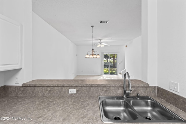 kitchen featuring tile patterned floors, ceiling fan with notable chandelier, white cabinets, sink, and decorative light fixtures