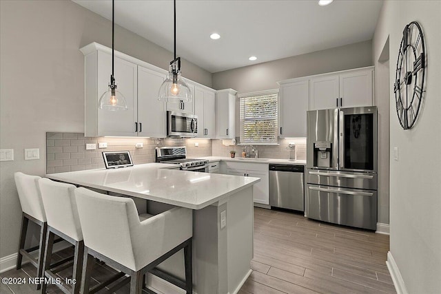 kitchen with white cabinets, a kitchen breakfast bar, hanging light fixtures, appliances with stainless steel finishes, and kitchen peninsula