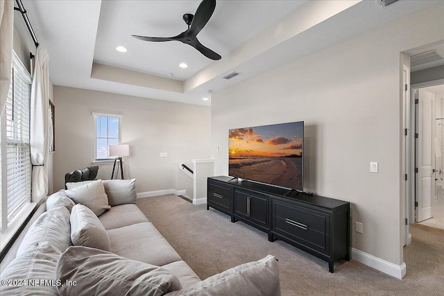 carpeted living room with a raised ceiling and ceiling fan