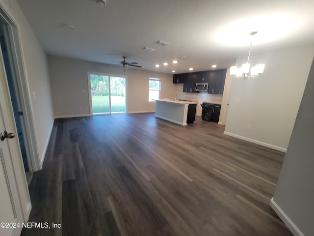 unfurnished living room with dark hardwood / wood-style floors, sink, and ceiling fan with notable chandelier