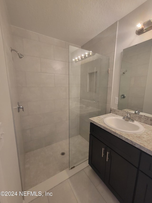 bathroom featuring tile patterned floors, vanity, tiled shower, and a textured ceiling