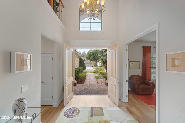 foyer entrance with light hardwood / wood-style floors, a towering ceiling, and an inviting chandelier