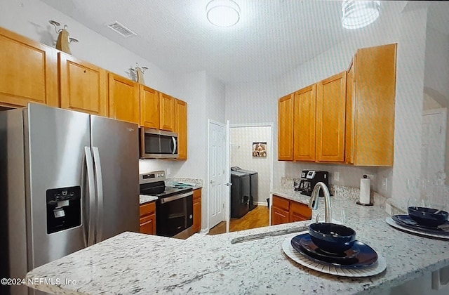 kitchen featuring light stone counters, stainless steel appliances, washer and clothes dryer, sink, and hardwood / wood-style floors