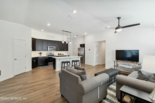 living room with a textured ceiling, light hardwood / wood-style floors, ceiling fan, and sink