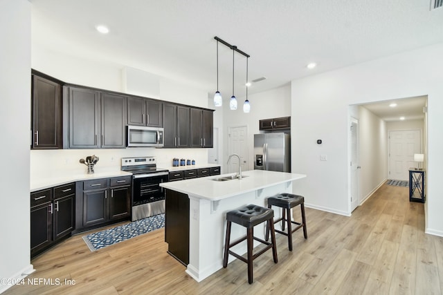 kitchen with a kitchen island with sink, hanging light fixtures, sink, light hardwood / wood-style floors, and stainless steel appliances