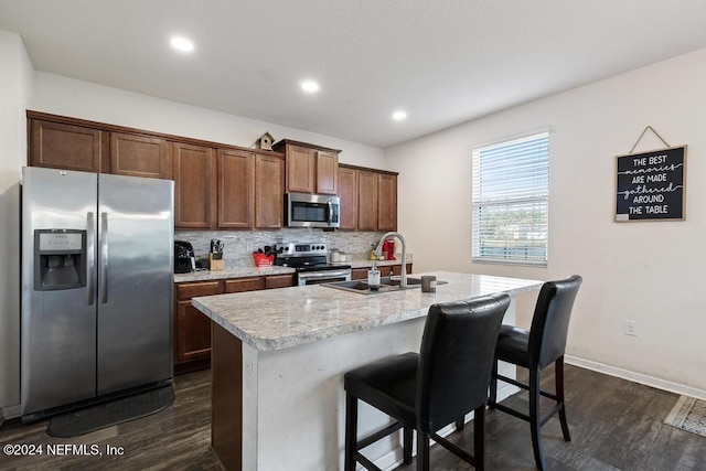 kitchen featuring sink, stainless steel appliances, dark hardwood / wood-style floors, an island with sink, and a breakfast bar