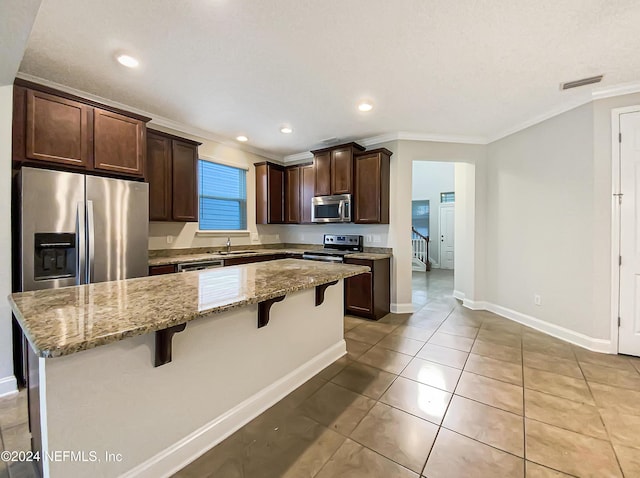 kitchen with light stone countertops, sink, stainless steel appliances, a breakfast bar area, and a kitchen island